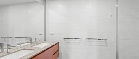 Un baño moderno con tres lavamanos, armarios de madera y cabina de ducha de vidrio.
