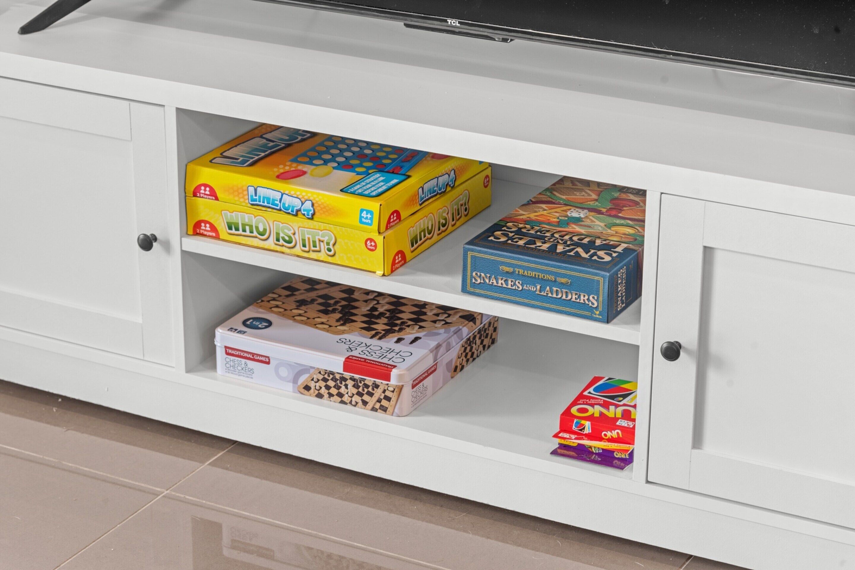 A cabinet with various board games including 'Who is it?' and 'Snakes and Ladders'.