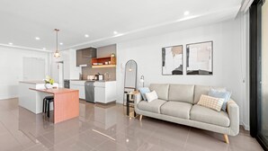 A modern living room with a sofa, a coffee table, and a kitchen area in the background. - Stylish West End Stay With Rooftop Pool & BBQ (Brisbane)