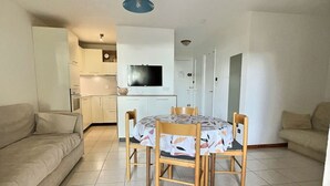 Un salon comprenant un canapé, une table à manger avec des chaises, un coin cuisine et un téléviseur fixé au mur.