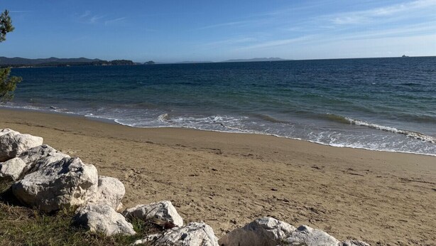 Une plage avec un ciel dégagé, une mer calme et des affleurements rocheux.