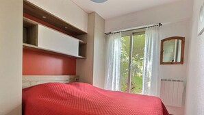 Une chambre à coucher avec un lit, une fenêtre avec des rideaux, un radiateur et un miroir.