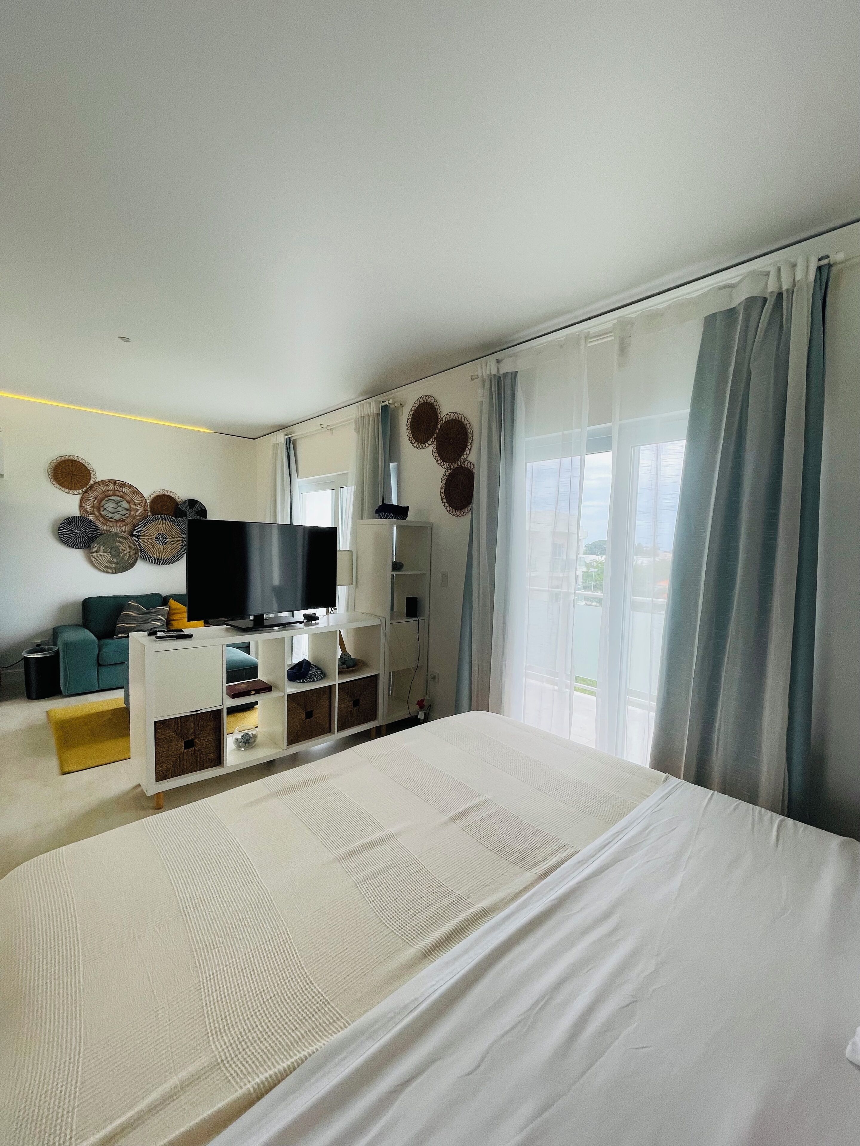 A modern hotel room with a large bed, a TV, a sofa, and a dining table.