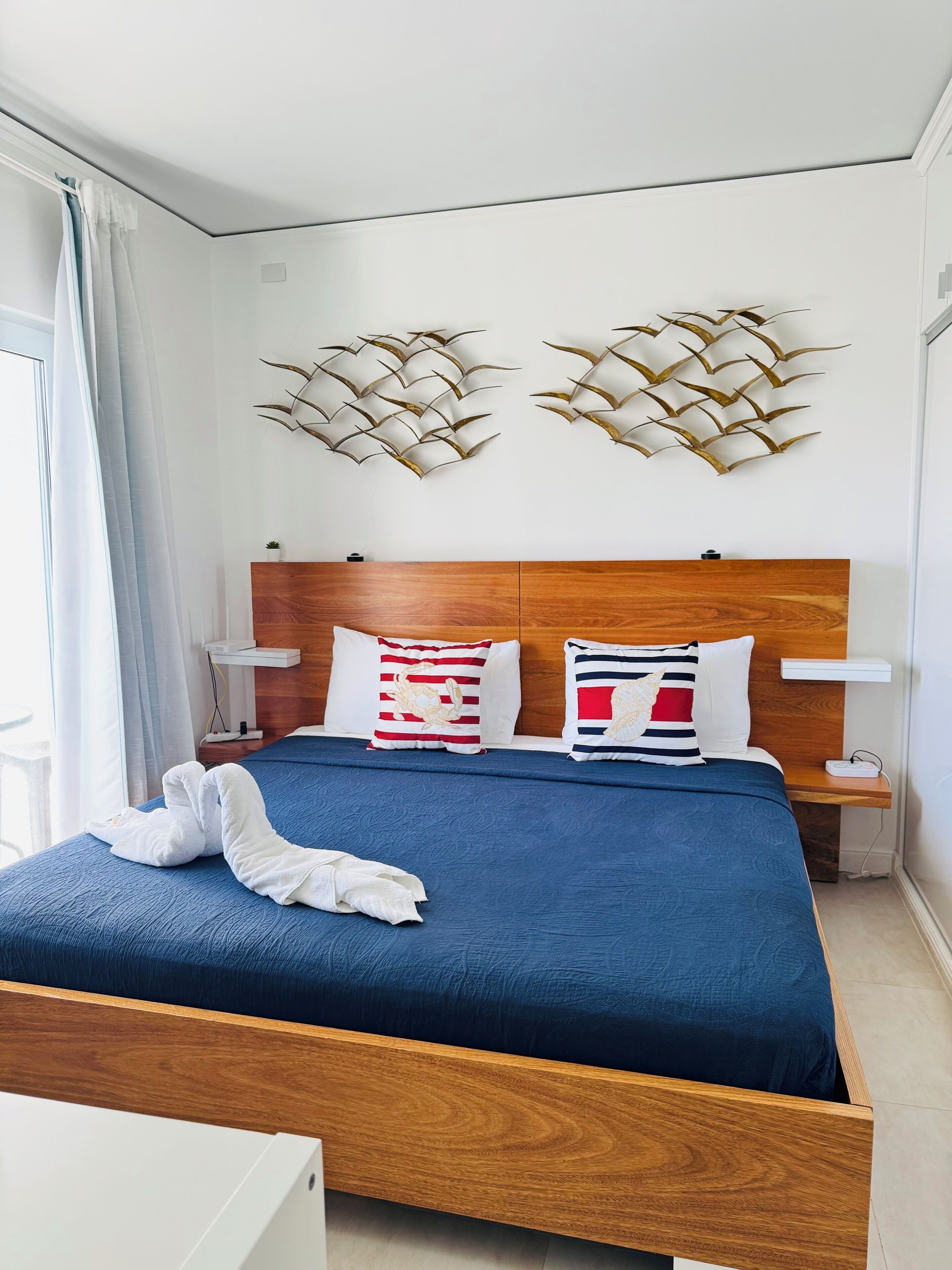 A modern hotel room with a wooden headboard, a blue bedspread, and two decorative wall art pieces.