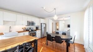 A modern kitchen with white cabinets, stainless steel appliances, and a wooden dining table with chairs. - Cozy Condo in Downtown Ludlow | Walk to Dining (Ludlow)