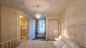 A bedroom with a bed, a chandelier, a window with curtains, and a door leading to a bathroom. - Cozy Condo in Downtown Ludlow | Walk to Dining (Ludlow)