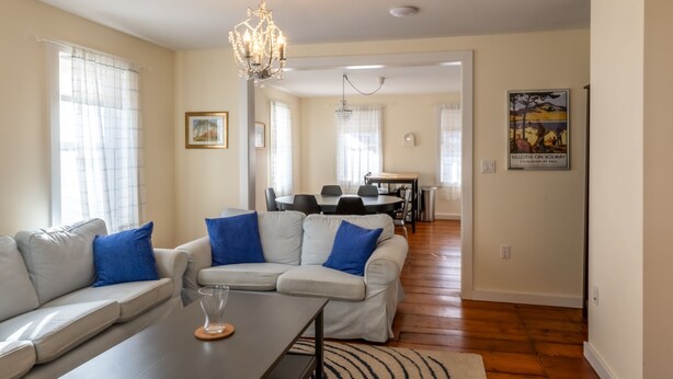 A modern living room with a sofa, a dining table, and a chandelier. - Cozy Condo in Downtown Ludlow | Walk to Dining (Ludlow)
