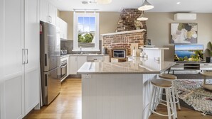 A modern kitchen with white cabinets, a stainless steel refrigerator, a brick oven, and a large island with stools. - Lovely 3-bed With Alfresco Dining in Prime Suburb (Ballarat)