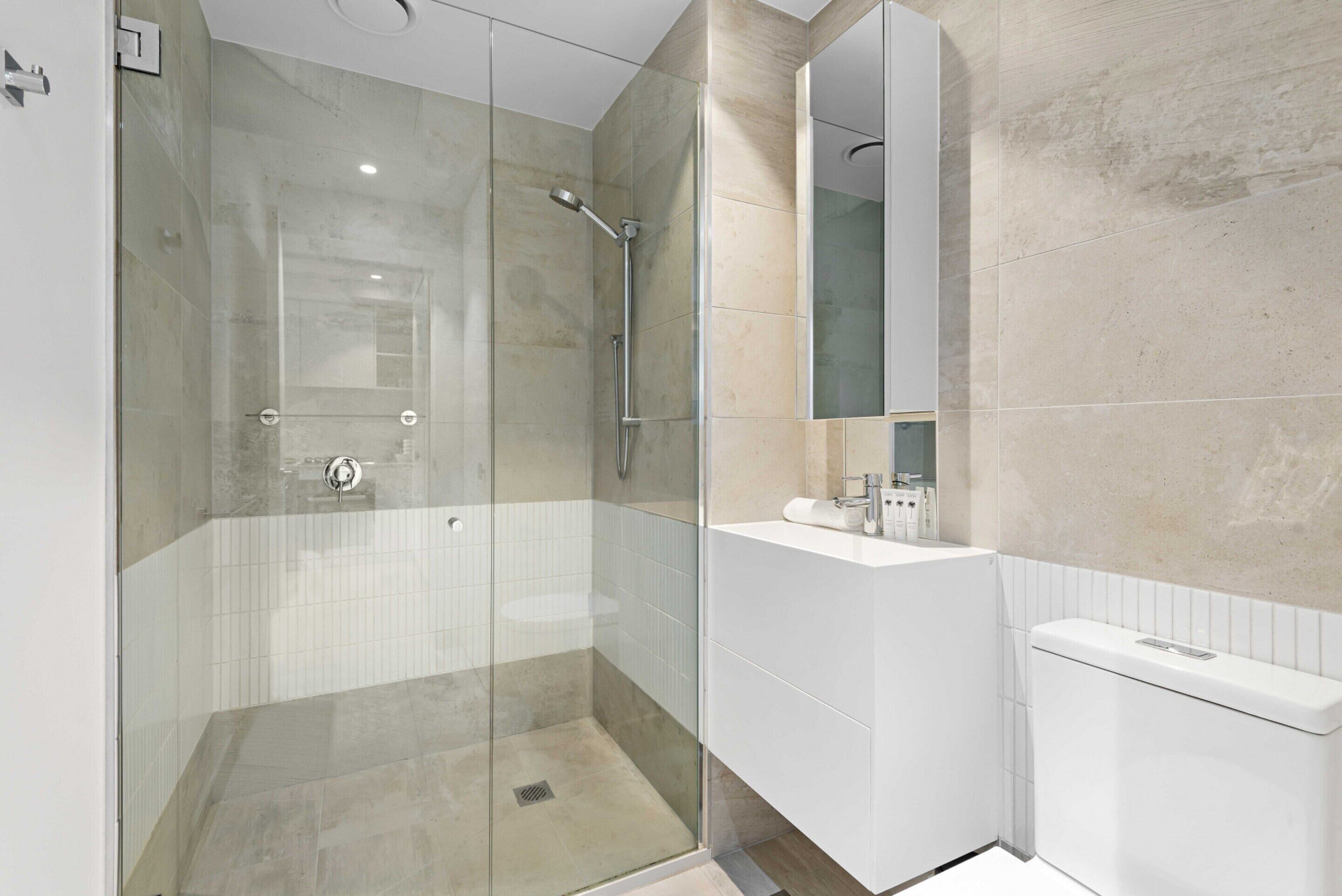 A modern bathroom with a glass-enclosed shower, a white sink, and a large mirror.