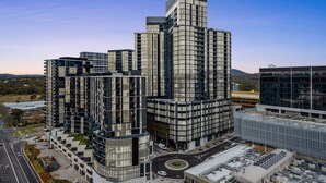 A modern high-rise building with a curved facade, multiple balconies, and a rooftop parking area.