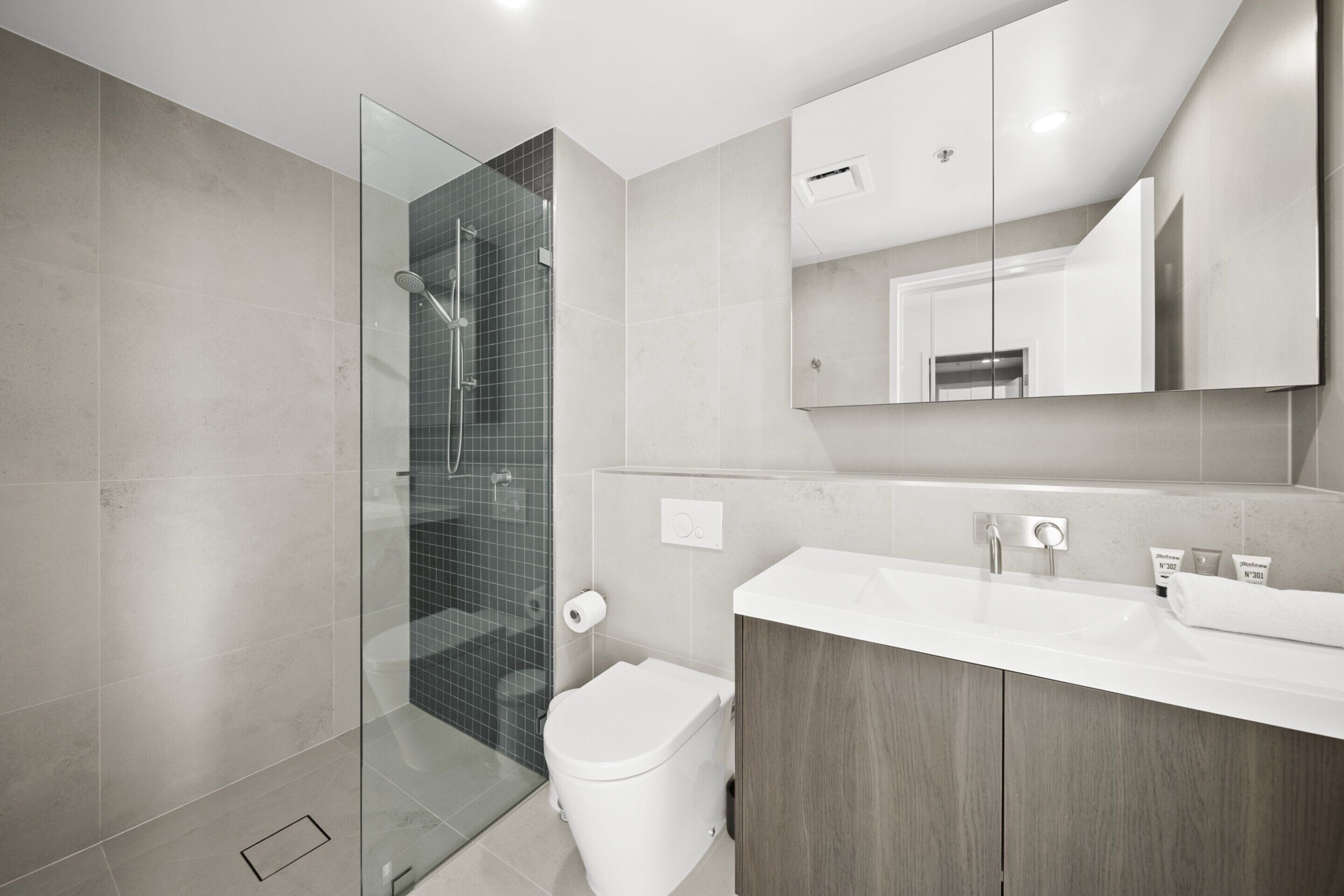 A modern bathroom with a glass shower enclosure, a white toilet, and a wooden vanity with a mirror above it.