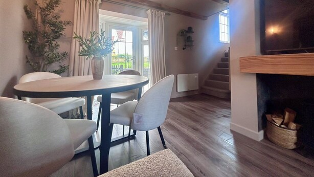 Un área de comedor con una mesa redonda, sillas y una planta en maceta. Una escalera conduce a un nivel superior.