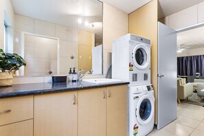 Een compacte keuken met een ingebouwde wasmachine en droger, een spoelbak en een potplant.