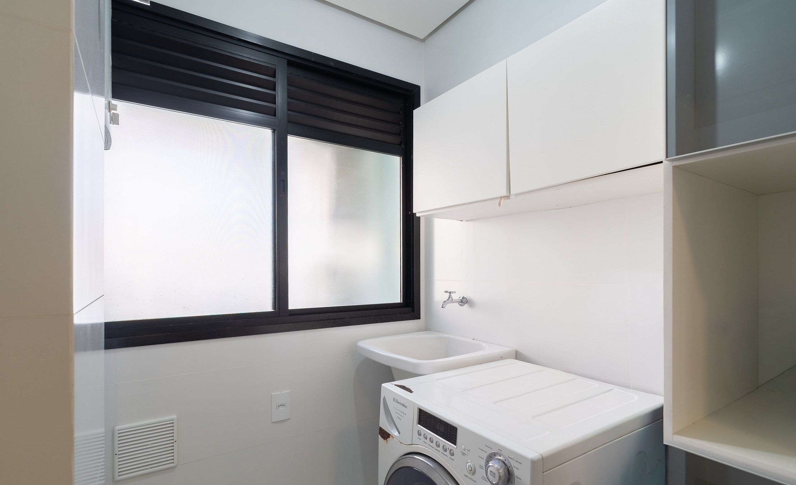 A laundry room with a washing machine, a sink, and a window with blinds.