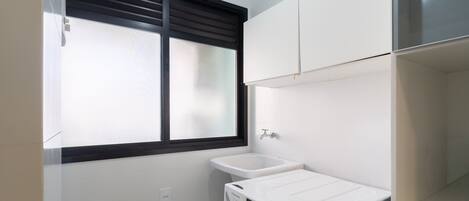 A laundry room with a washing machine, a sink, and a window with blinds.