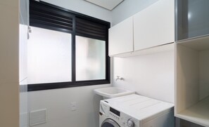 Une buanderie équipée d’un lave-linge, d’un évier et d’une fenêtre avec des stores.