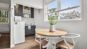 Eine moderne Küche mit weißen Schränken, einer Mikrowelle und einem Kühlschrank. Ein Esstisch mit Stühlen und eine Vase mit Pflanze sind ebenfalls vorhanden.