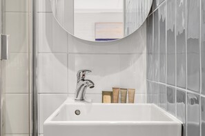 Uma casa de banho com uma pia branca, uma torneira cromada e um espelho em cima. Há três frascos de produtos de higiene na pia.