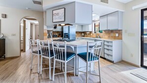 A modern kitchen with a central island, white cabinetry, and a 'STAY' sign above the island. - HavaHappyStay | Near Lake and Golf~RV/Boat Parking (Lake Havasu City)