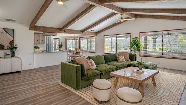 Ein geräumiges Loft mit freiliegenden Holzbalken, einem grünen Sofa, einem Esstisch und großen Fenstern.