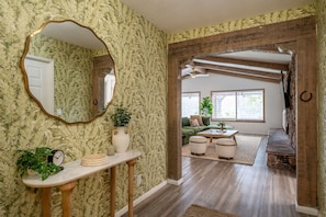 A hallway with a mirror, a clock, a vase, and a plant on a console table.
