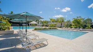 A pool area with lounge chairs and umbrellas, surrounded by greenery and buildings. - Fantastic apartment with AC in Green one, Playa Dorada (Playa dorada)