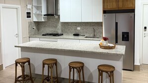 A modern kitchen with white cabinets, a granite countertop, a stainless steel refrigerator, and four wooden stools. - Fantastic apartment with AC in Green one, Playa Dorada (Playa dorada)