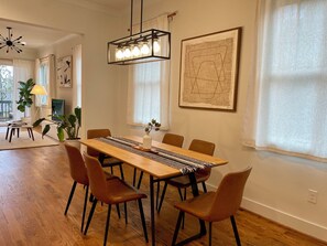 Un coin repas avec une longue table en bois, six chaises et un lustre moderne.