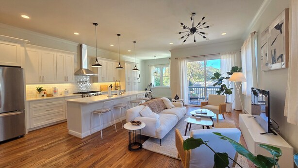 A modern kitchen with white cabinetry, a central island, and a dining area with a white sofa and coffee table. - Grant Park Retreat - Steps to Zoo, & Great Eats (Atlanta)