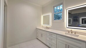 Une salle de bain moderne avec deux lavabos, un grand miroir et une fenêtre située au-dessus du miroir.