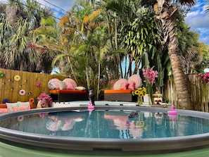 Un área de piscina con cubierta de madera, una silla de descanso y diversas plantas.