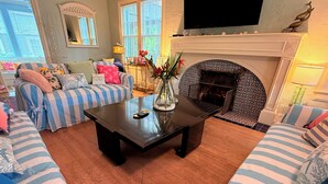 Ein Wohnzimmer mit gestreiften Sofas, einem Kamin, einem Fernseher und einer Vase mit Blumen.