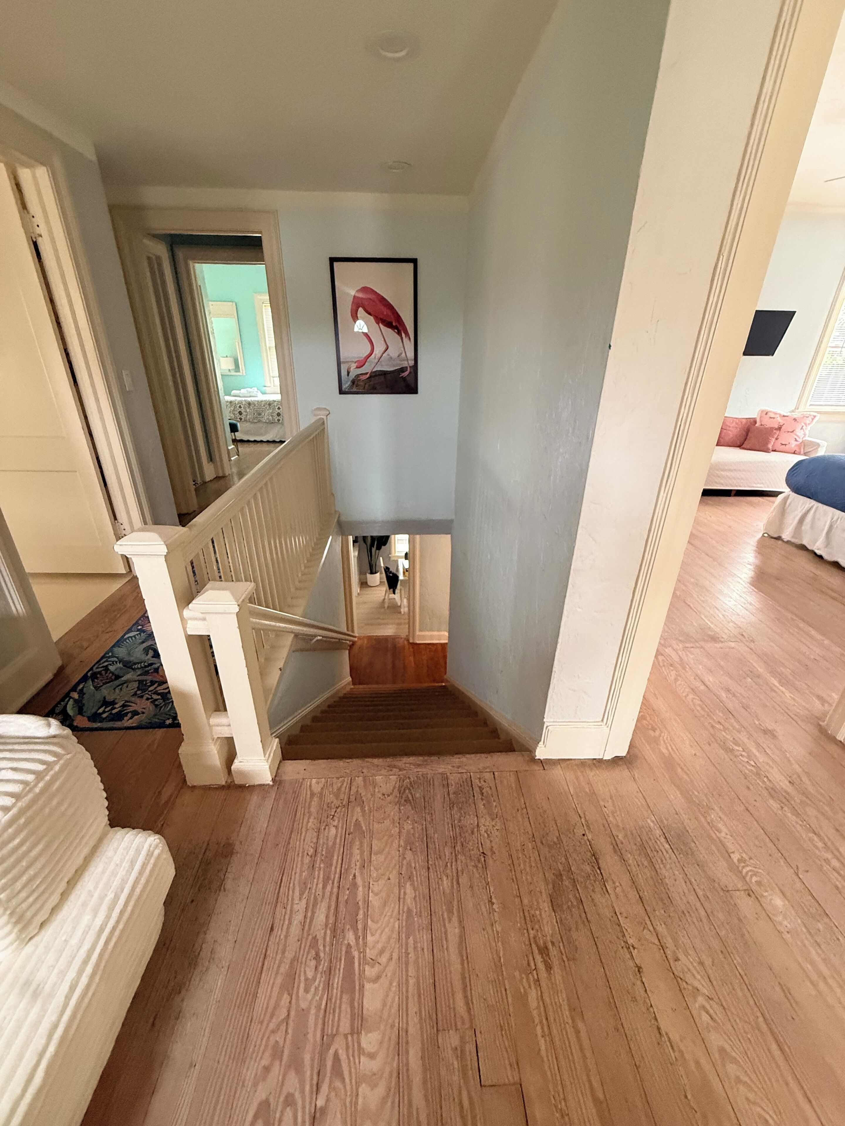 Een trap die leidt naar een slaapkamer met een bed, een ingelijst beeld aan de muur en een houten vloer.