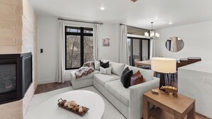 A modern living room with a fireplace, a sectional sofa, a dining area, and a large window. - Luxury retreat: hot tub, steam shower, 2-bed 2-bath on the Blue River. (Silverthorne)