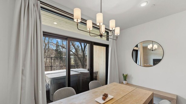 A modern dining area with a wooden table, chairs, a chandelier, and a large mirror on the wall. - Luxury retreat: hot tub, steam shower, 2-bed 2-bath on the Blue River. (Silverthorne)