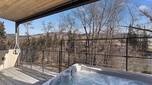 A hot tub on a wooden deck with a view of trees and hills. - Luxury retreat: hot tub, steam shower, 2-bed 2-bath on the Blue River. (Silverthorne)