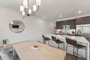 Uma cozinha moderna com uma ilha central, eletrodomésticos embutidos e uma área de refeições com mesa redonda e banquetas de bar.