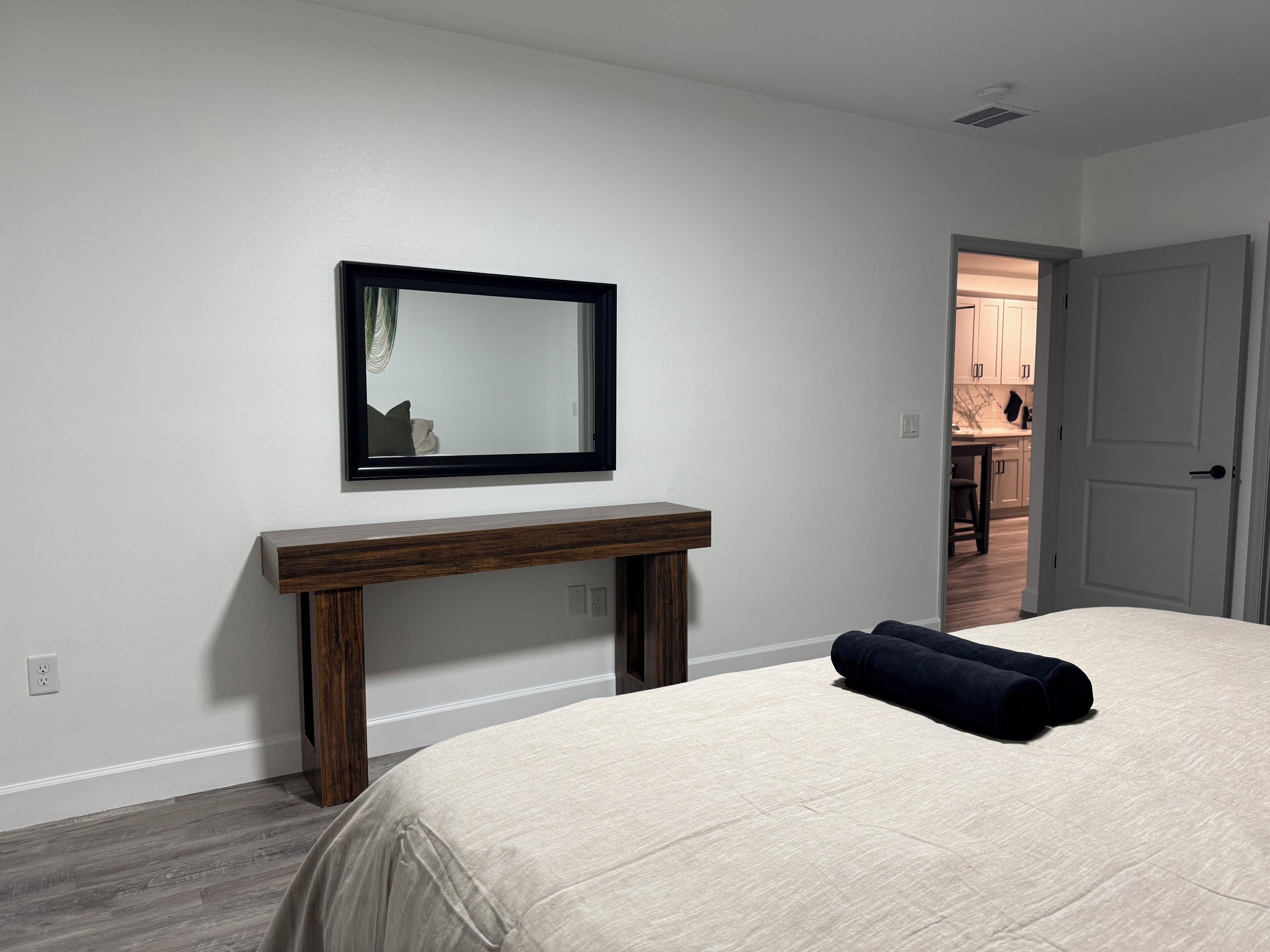 A bedroom with a bed, a bedside table, a mirror, and a door leading to a bathroom.