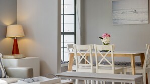 A modern living room with a white dining table, white chairs, a red lamp, and a painting of a beach scene. - Coastal Retreat on Hazel - Lakes Entrance Getaway (Kalimna)