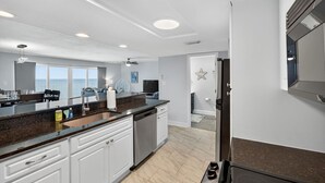 A modern kitchen with white cabinets, a granite countertop, and a built-in dishwasher. - Updated 2 bed 2 bath Beachfront Condo with Pool and Amazing Water Views (Indian Shores)