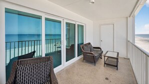 A balcony with a view of the beach, wicker furniture, and a door. - Updated 2 bed 2 bath Beachfront Condo with Pool and Amazing Water Views (Indian Shores)