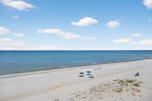 A beach with clear skies, calm waters, and a few umbrellas and lounge chairs.