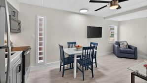 A modern kitchen with a built-in oven, a dining area with a table and chairs, a ceiling fan, and a TV mounted on the wall. - Your Gulf Coast Escape in Madeira Beach (St. Petersburg)