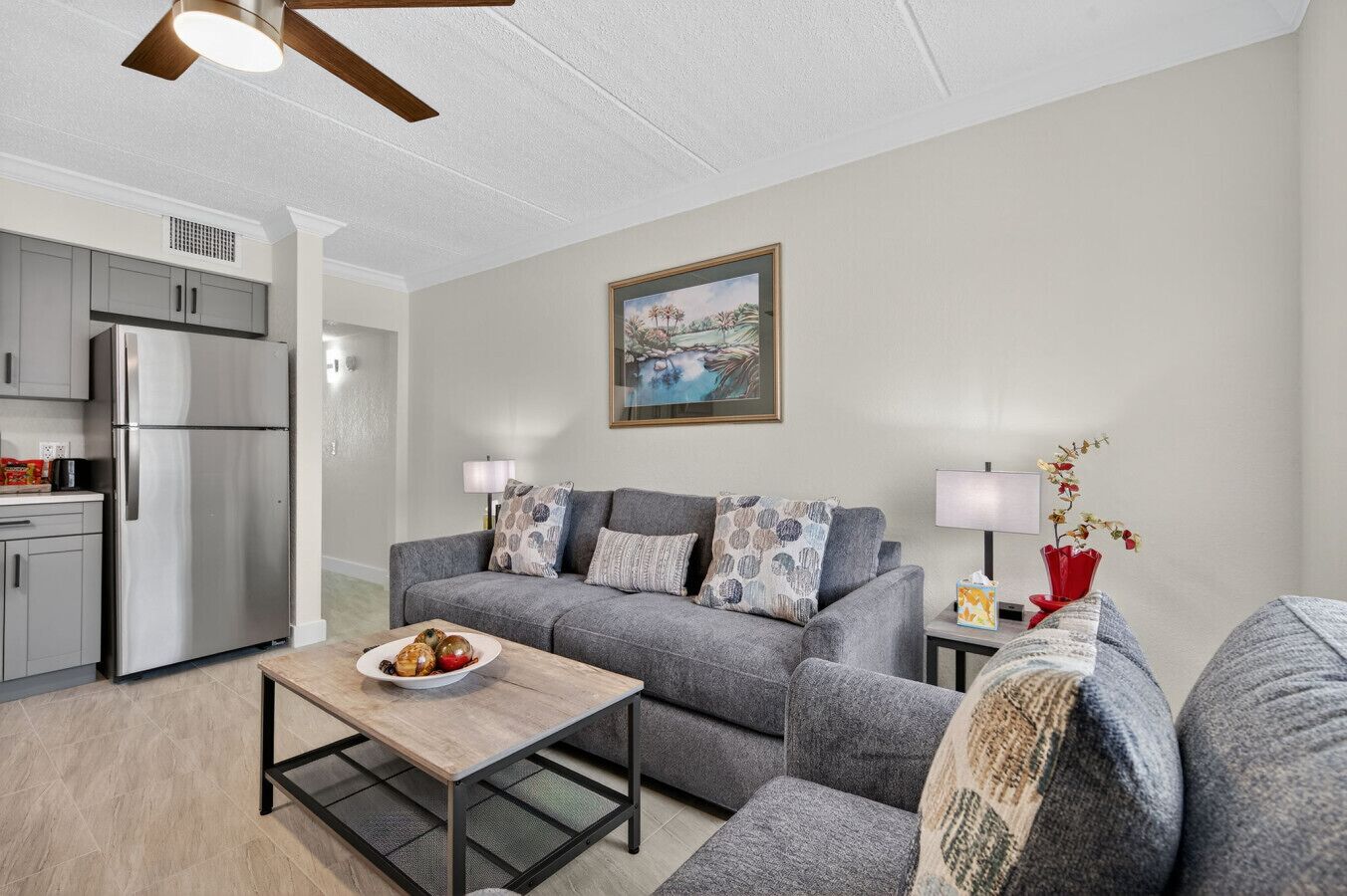 A modern living room with a grey sofa, a coffee table, and a kitchen area with a refrigerator.