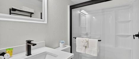 A modern bathroom with a large sink, mirror, and a glass shower enclosure.