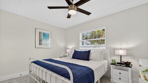 A bedroom with a bed, bedside tables, a ceiling fan, a window with blinds, and a framed picture on the wall. - Coastal Comfort Just Steps from the Sand (St. Petersburg)