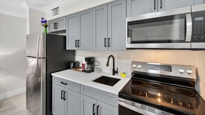 A modern kitchen with grey cabinets, a stainless steel refrigerator, a microwave, and an oven. - Coastal Comfort Just Steps from the Sand (St. Petersburg)