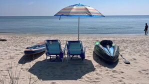 A beach with two lounge chairs, a colorful striped umbrella, and two kayaks.