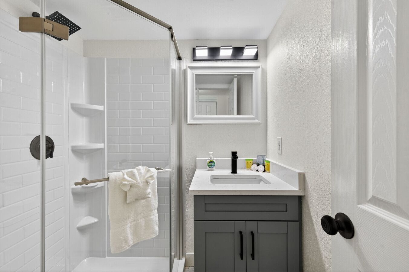 A bathroom with a glass shower enclosure, a white sink with a mirror above it, and a towel hanging on a rack.