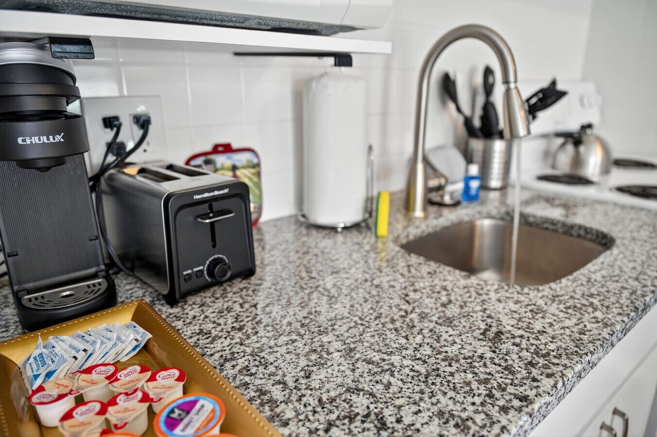 A kitchen with a toaster, coffee maker, sink, and a box of yogurt.